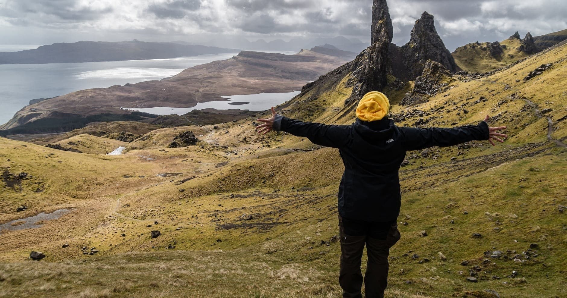 Person with arms raised on hilltop enjoying Scottish landscape