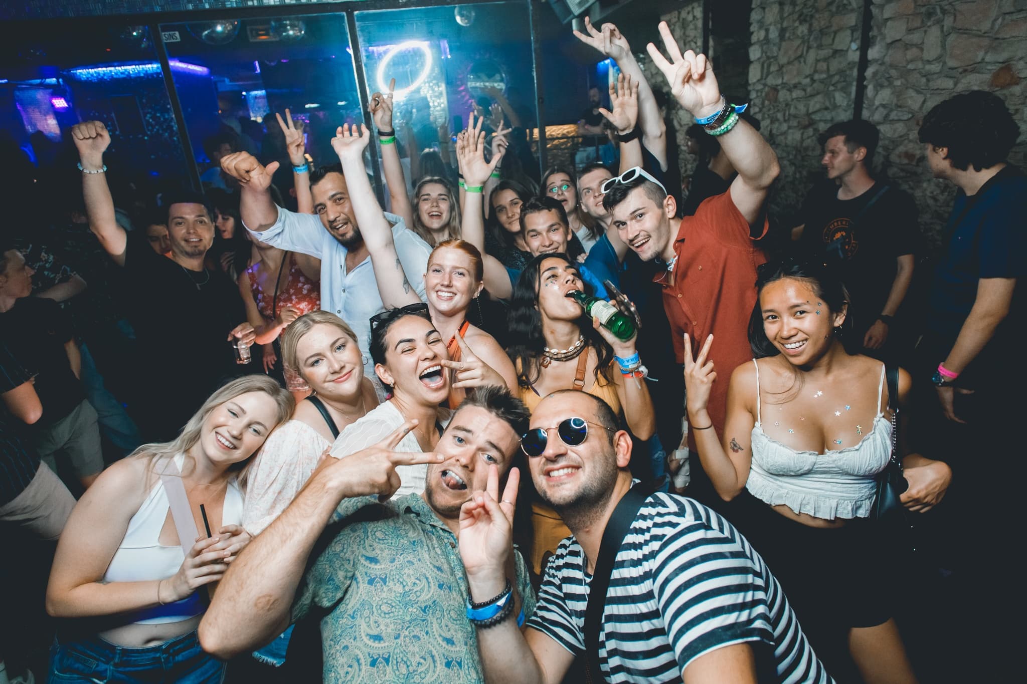 Energetic dance crowd posing at crowded nightclub with neon