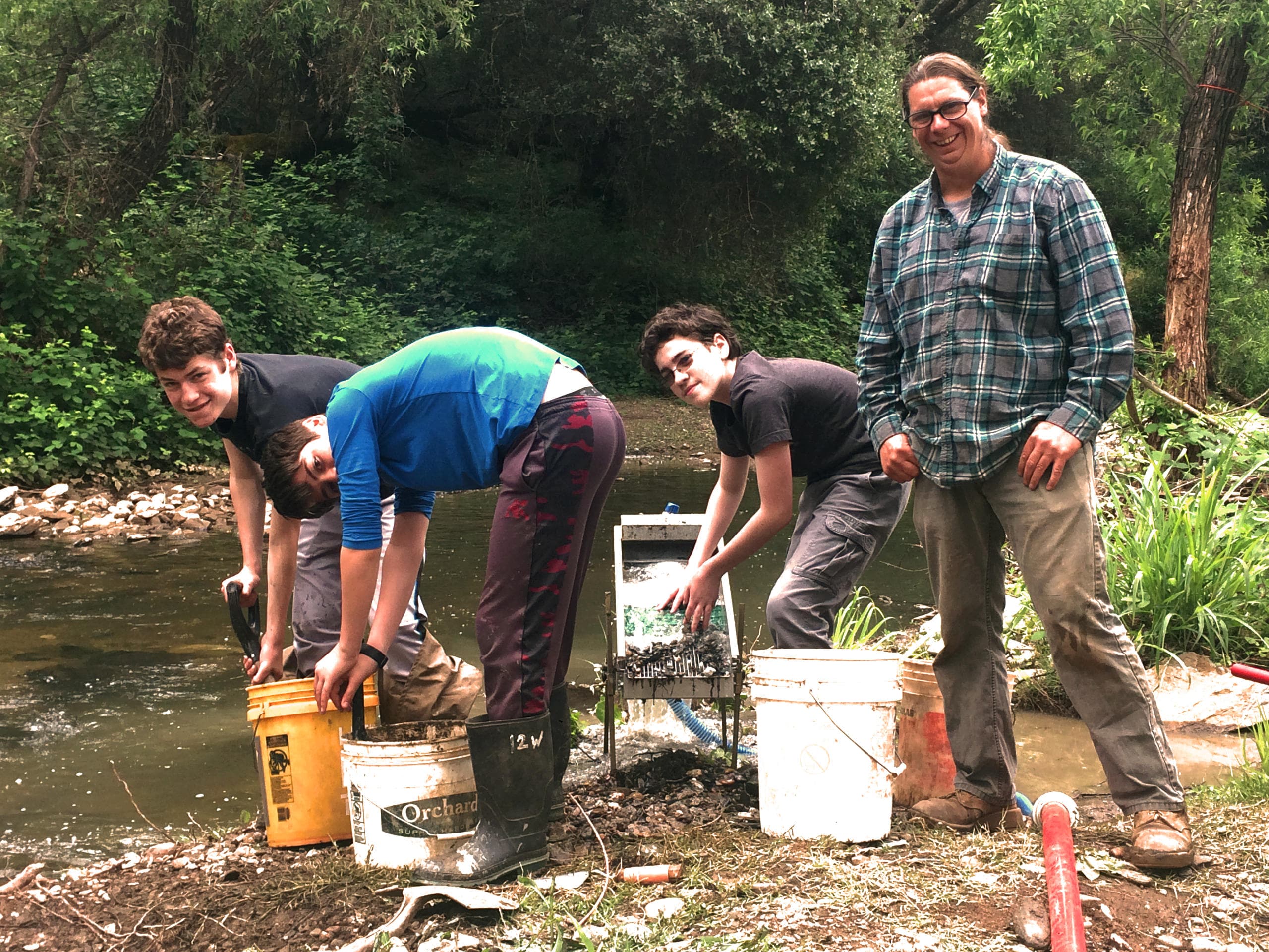 Crew prospecting and panning at rocky stream, group outdoor work