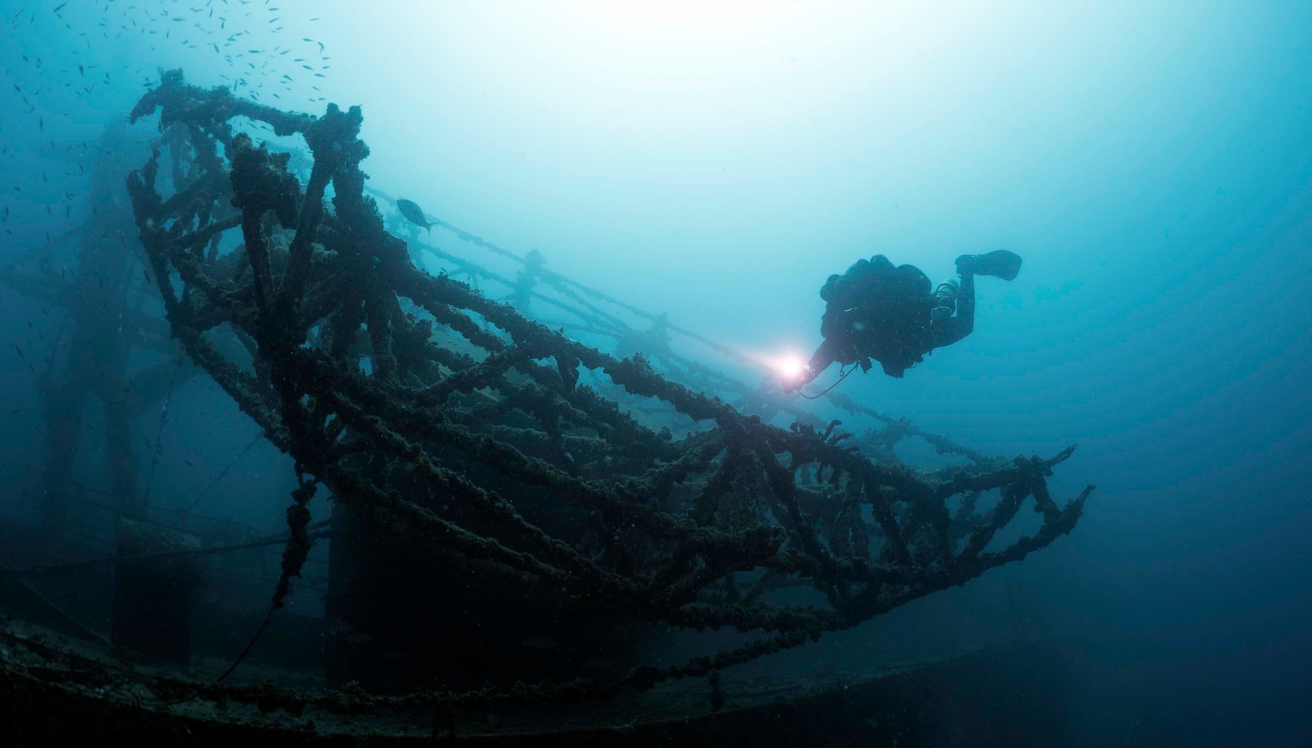 Scuba diver silhouetted exploring submerged wreck at depth