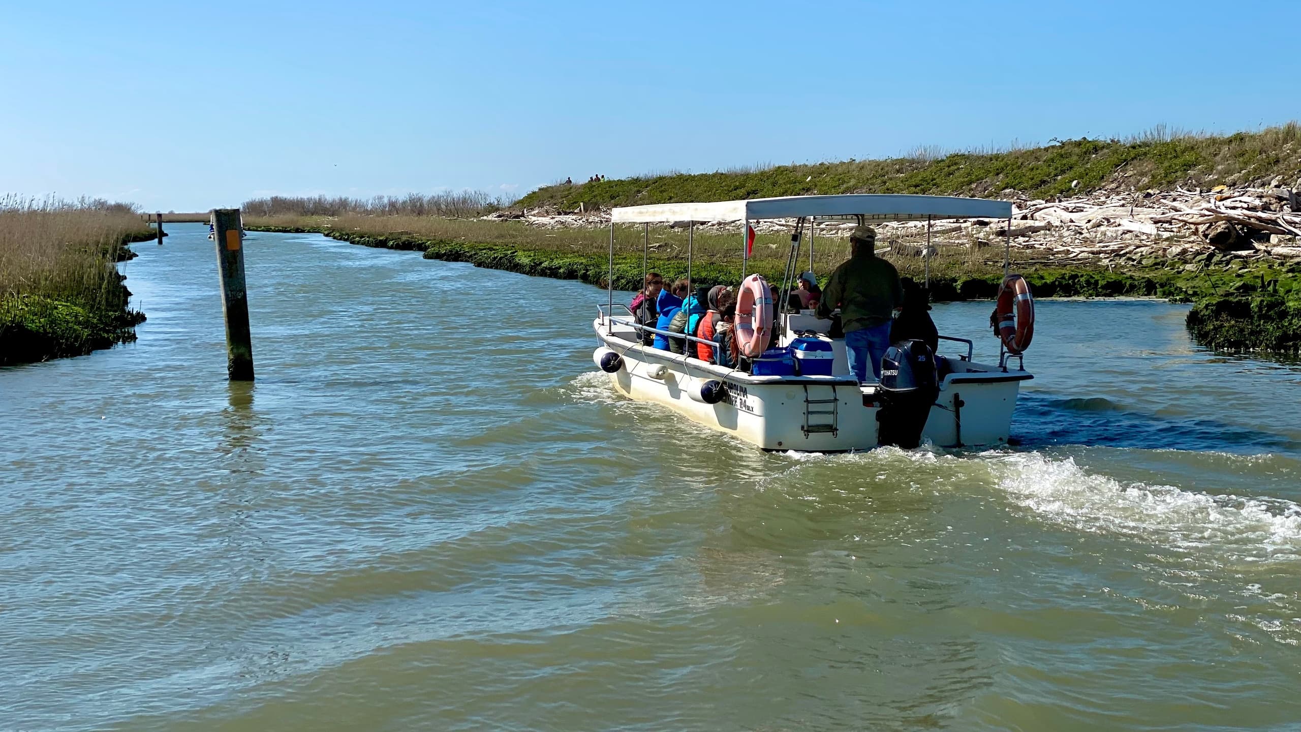 Small motorboat cruising a narrow lagoon channel with marshland