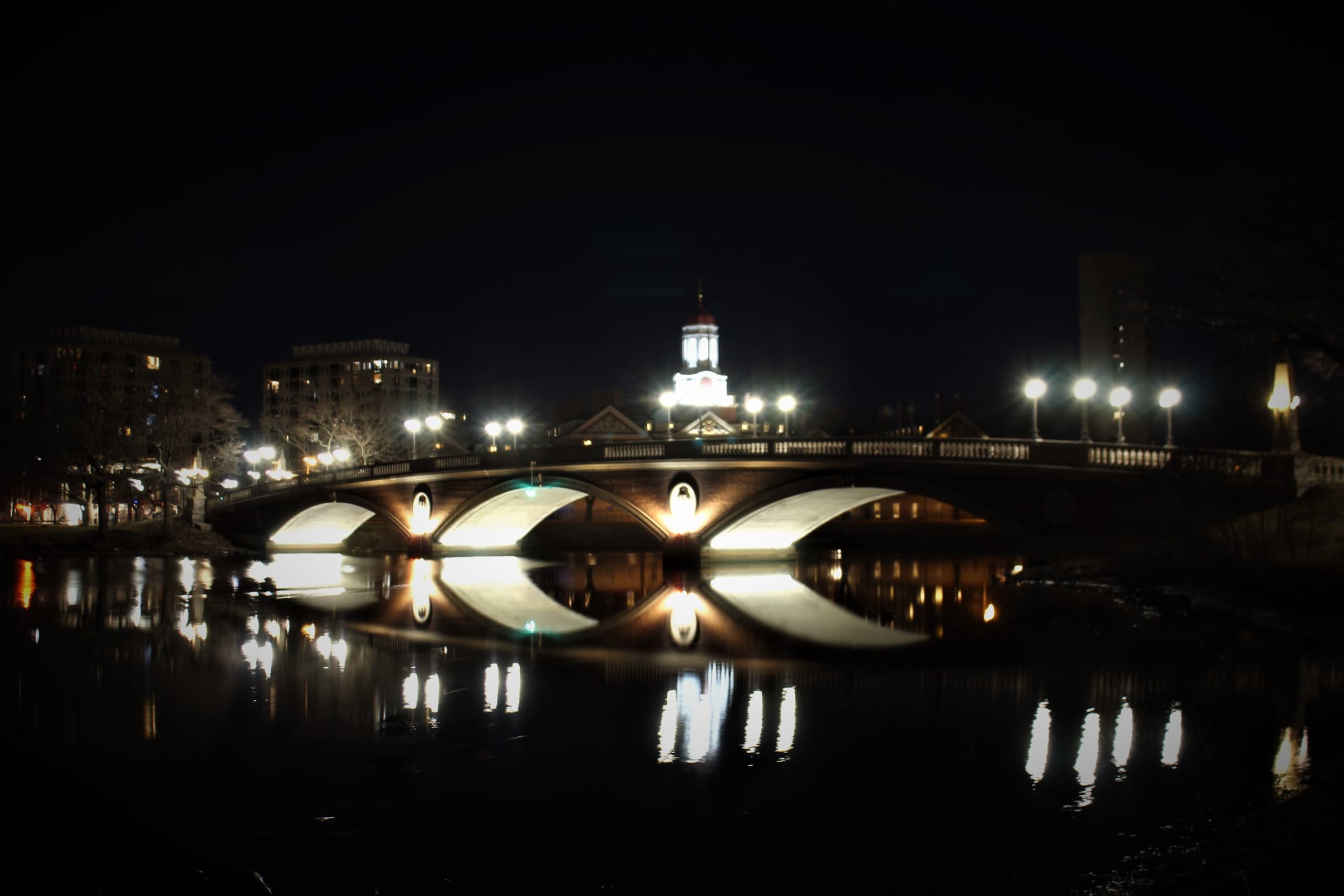 Illuminated city bridge reflecting on river at night