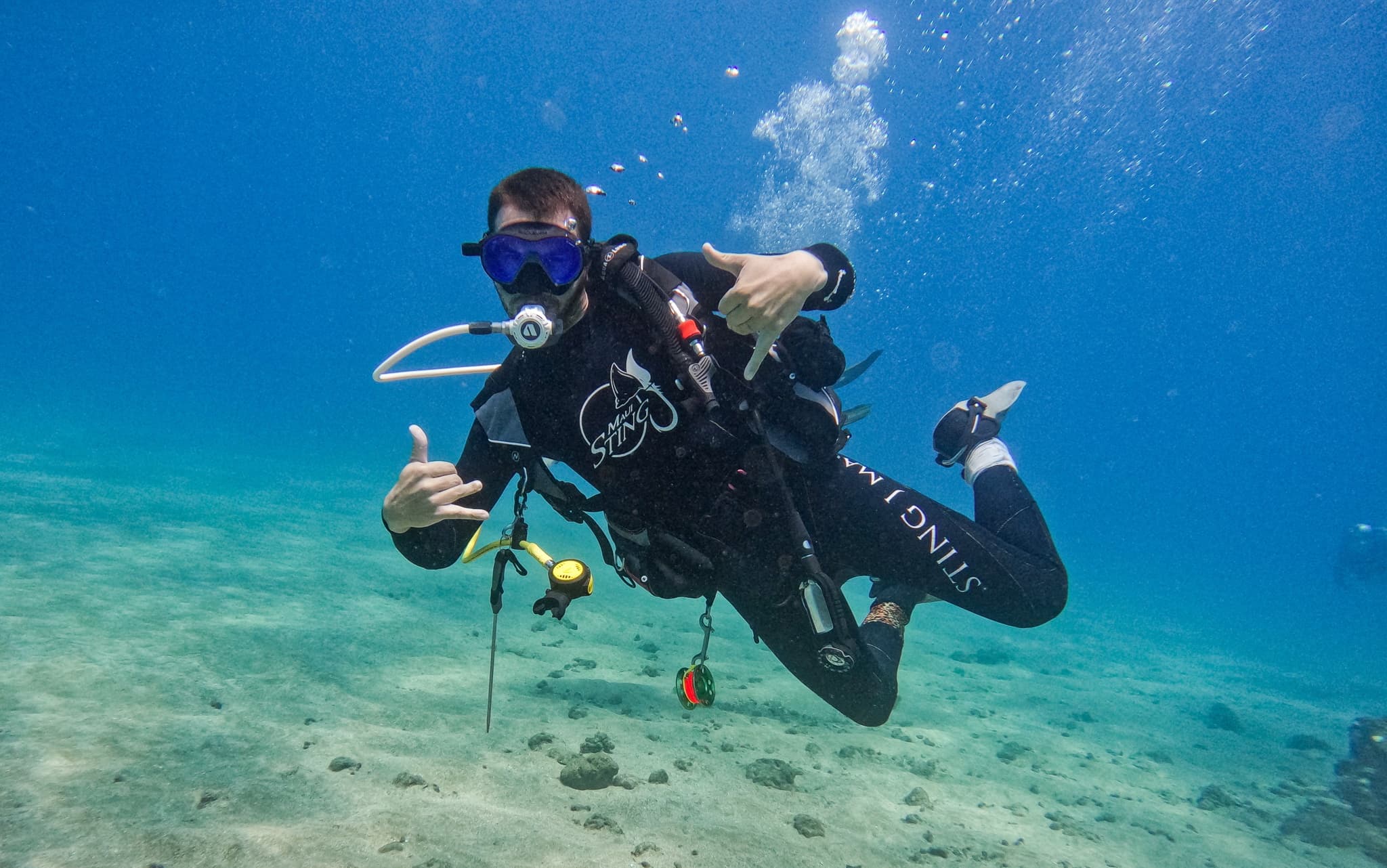 Scuba diver giving thumbs-up above sandy seabed, clear tropical water