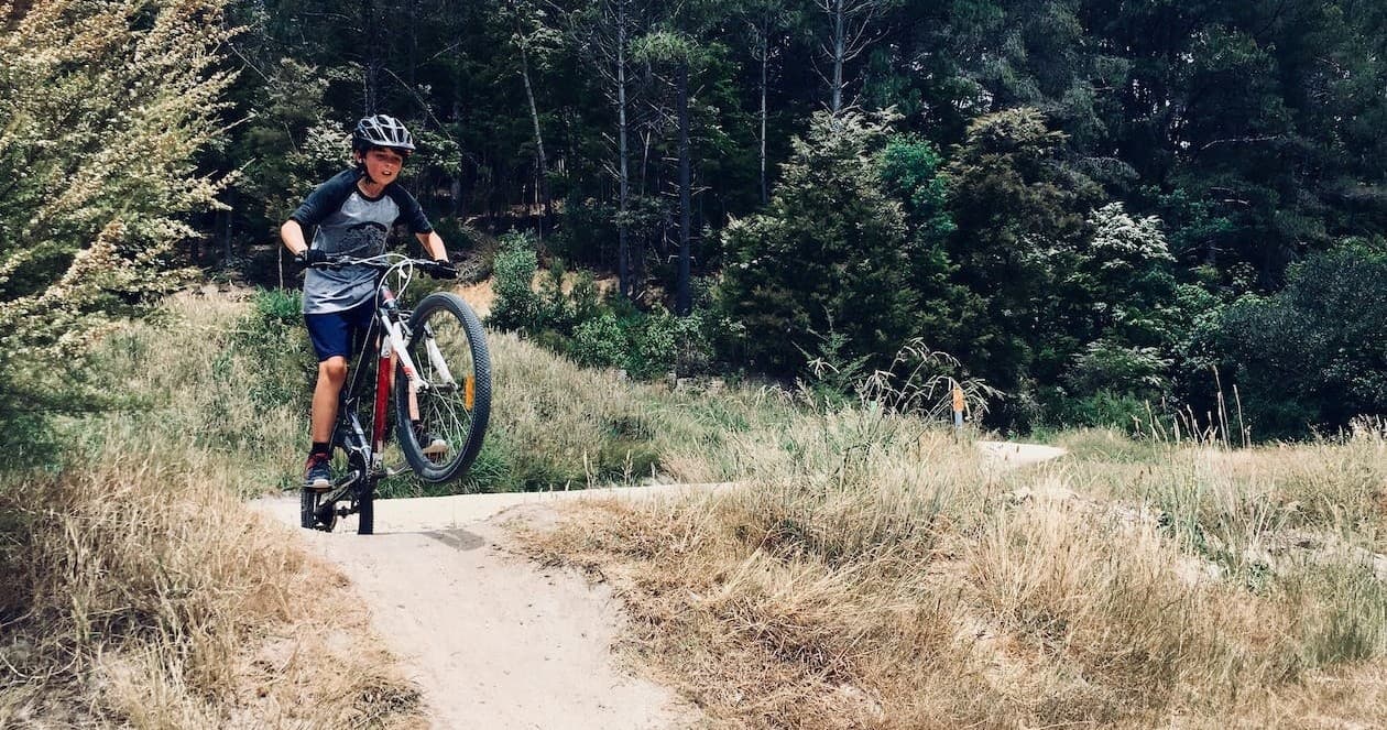 Young rider performing wheelie on dirt trail through forested singletrack