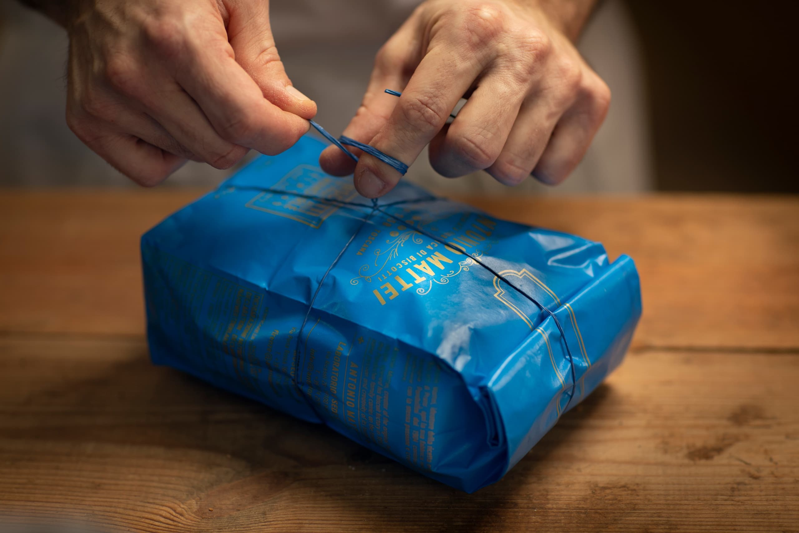 Hands tying blue parcel on wooden table indoors, gift wrapping