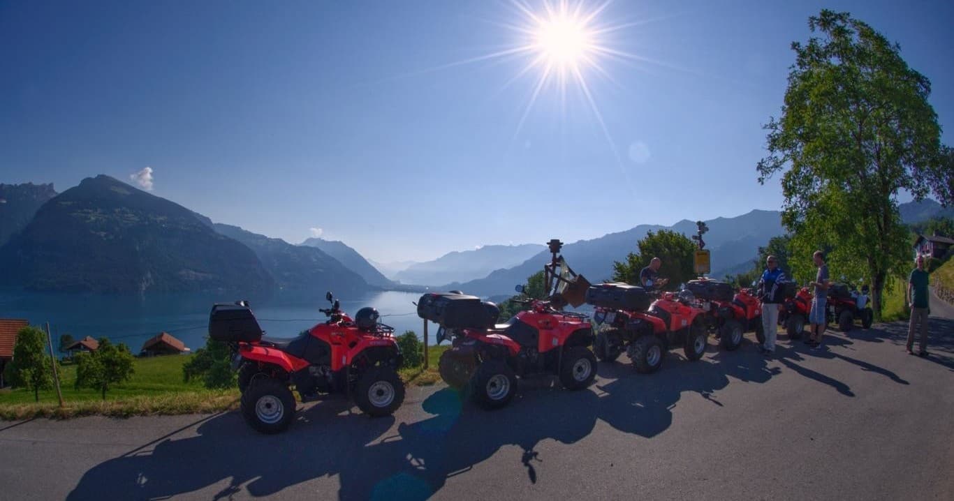 Group of quads on lakeside alpine road with sunlit mountains