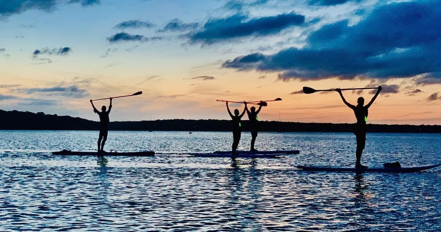 Silhouetted paddleboarders practicing yoga at sunset on ocean