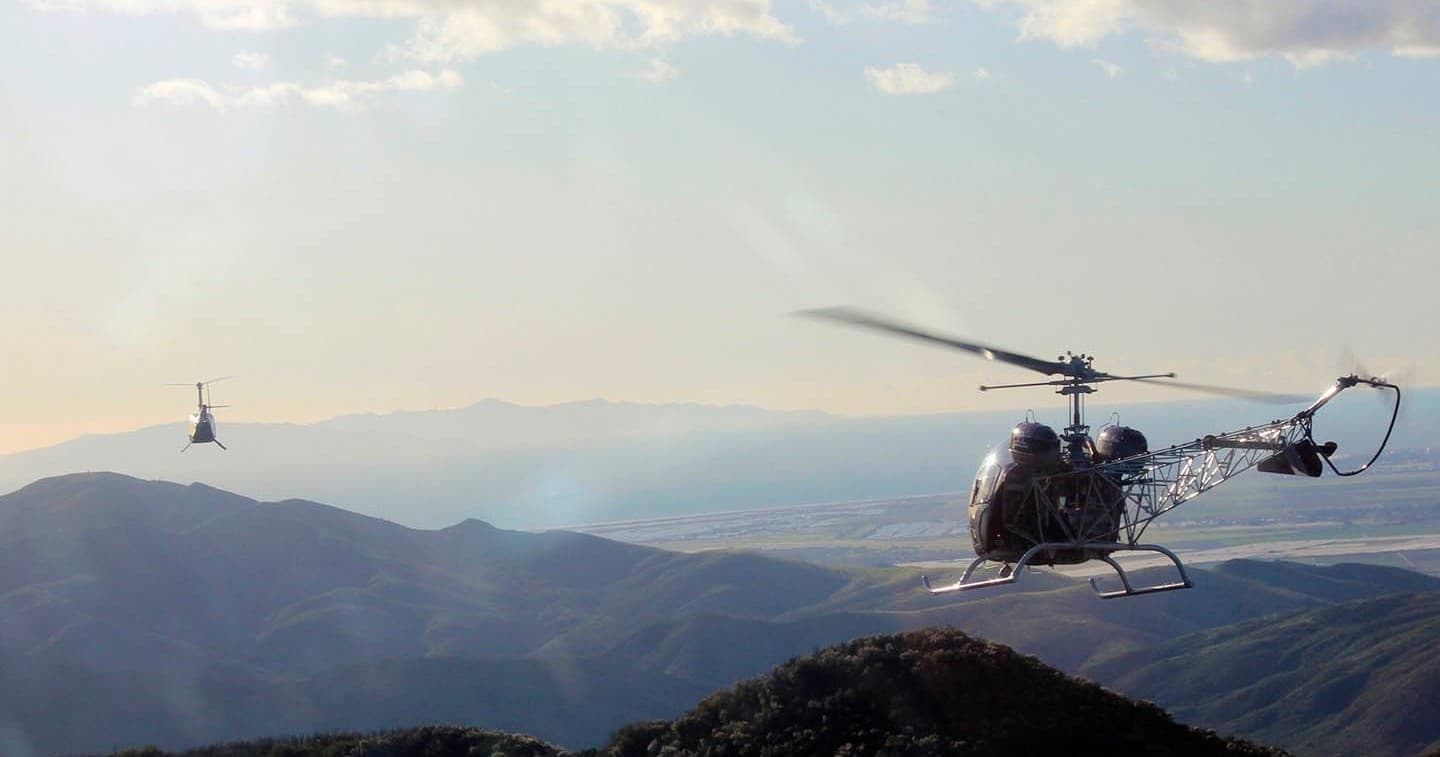 Two helicopters flying over mountainous terrain during tour