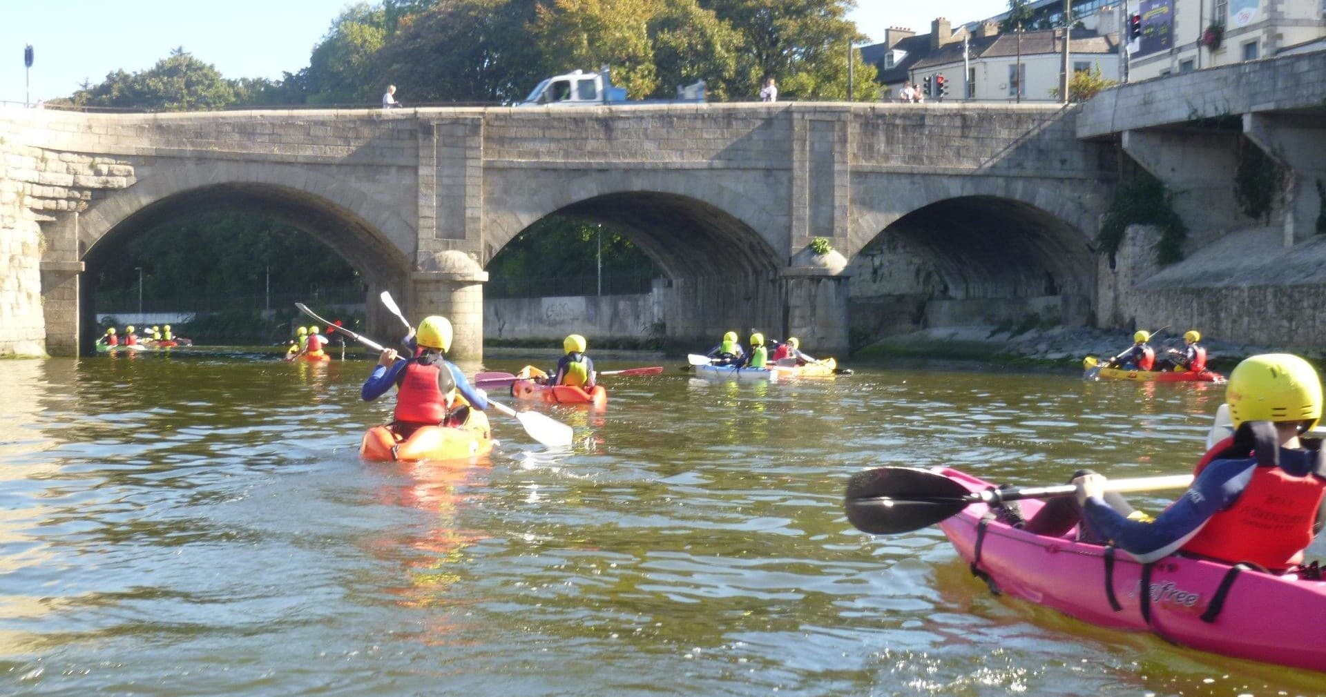 Kayakers navigating river under historic stone bridge in town