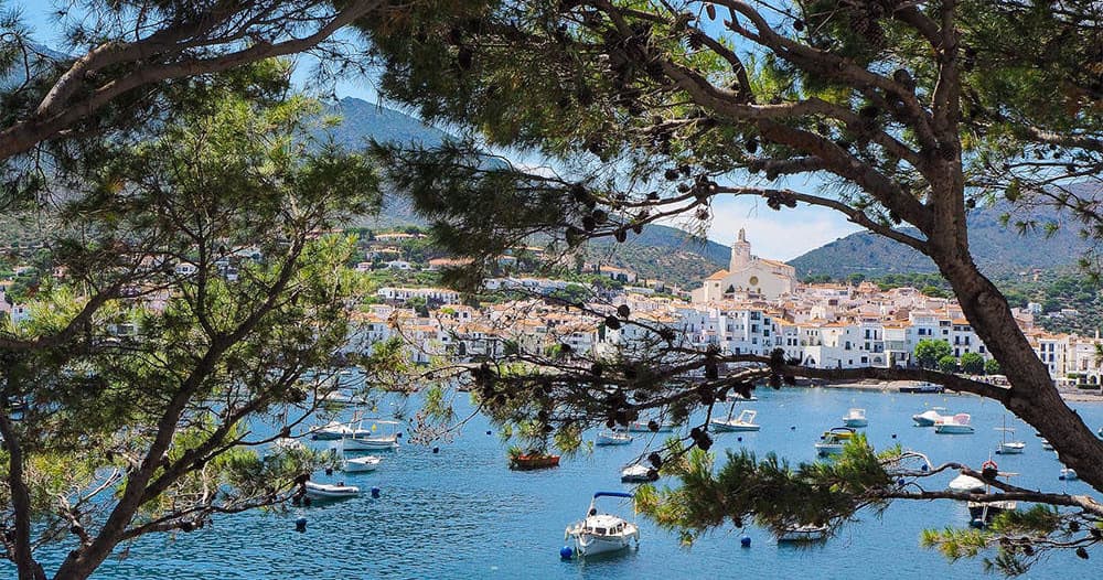 Coastal cove with anchored boats framed by pine trees, Cadaqués