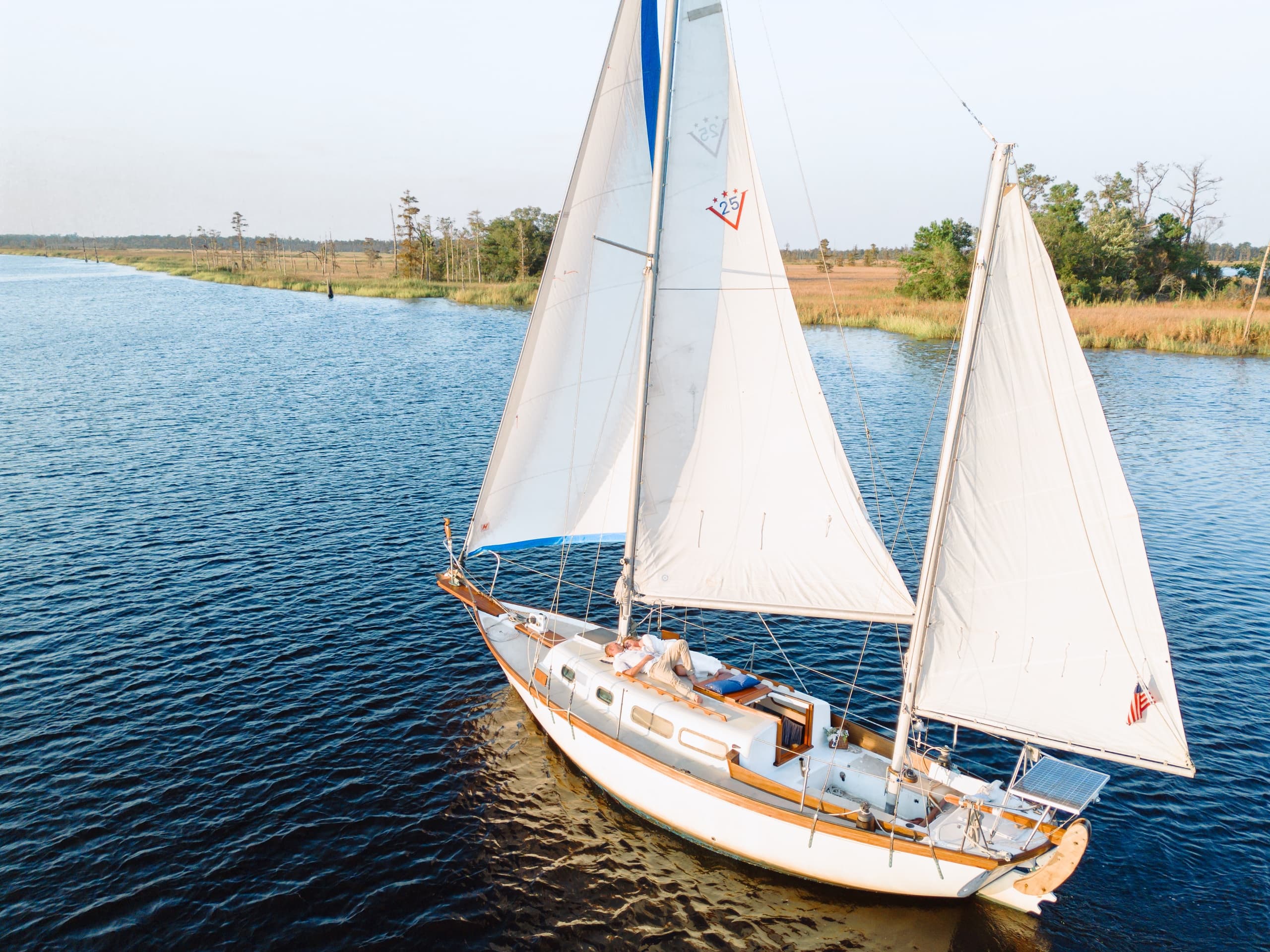 Aerial sailboat sailing on blue river with full white sails