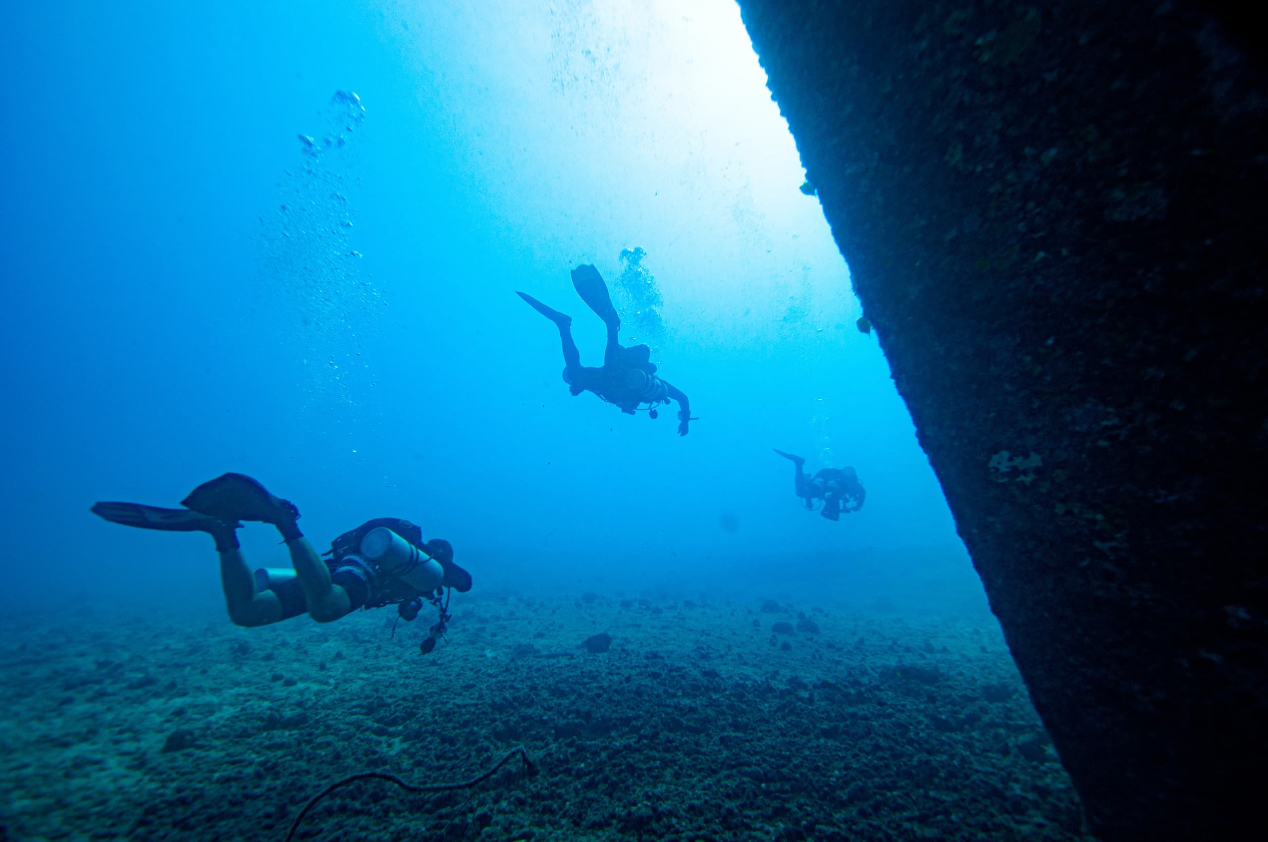 Scuba divers silhouetted near underwater wall in open ocean