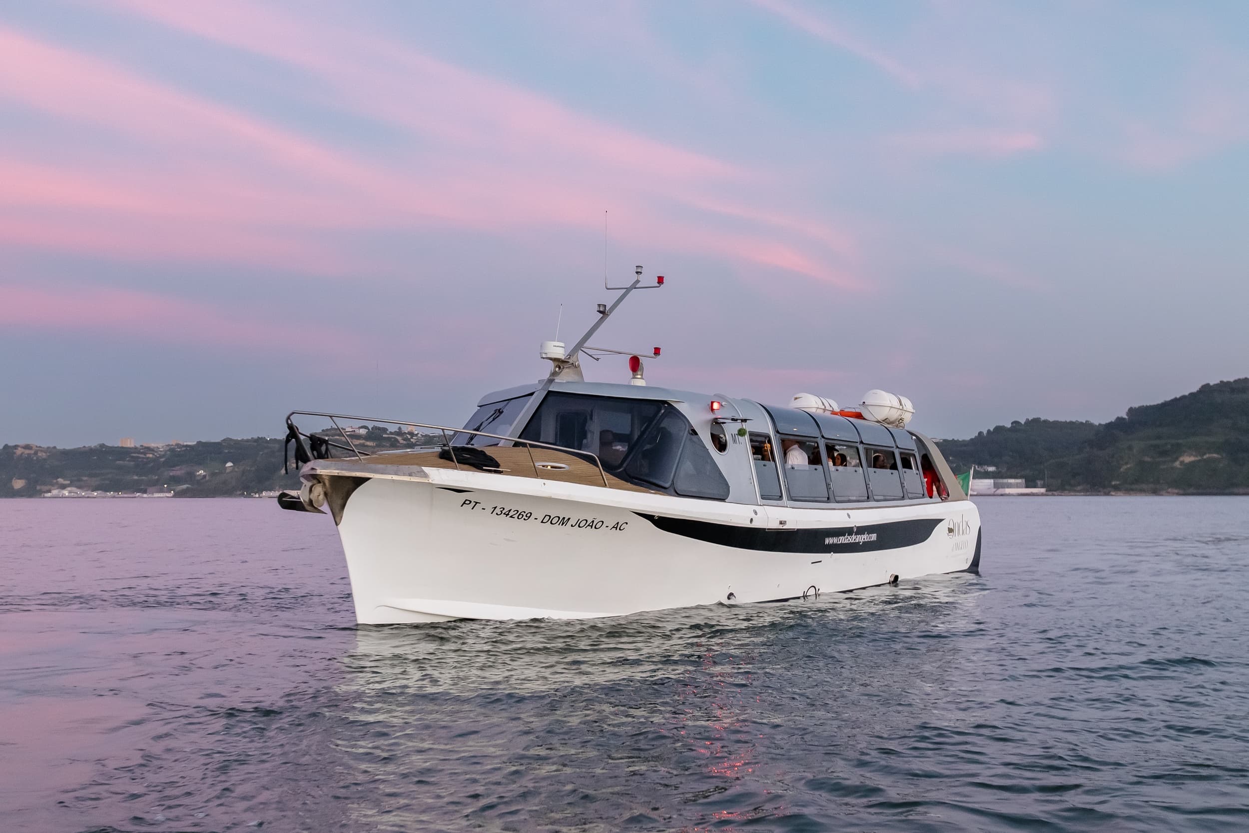 White passenger boat cruising calm pink-sky coastal waters