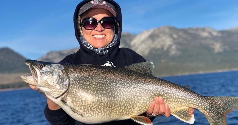 Angler presenting large lake trout with mountain backdrop