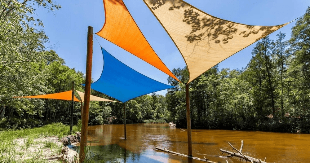 Colorful shade sails over calm river in forested paddling area