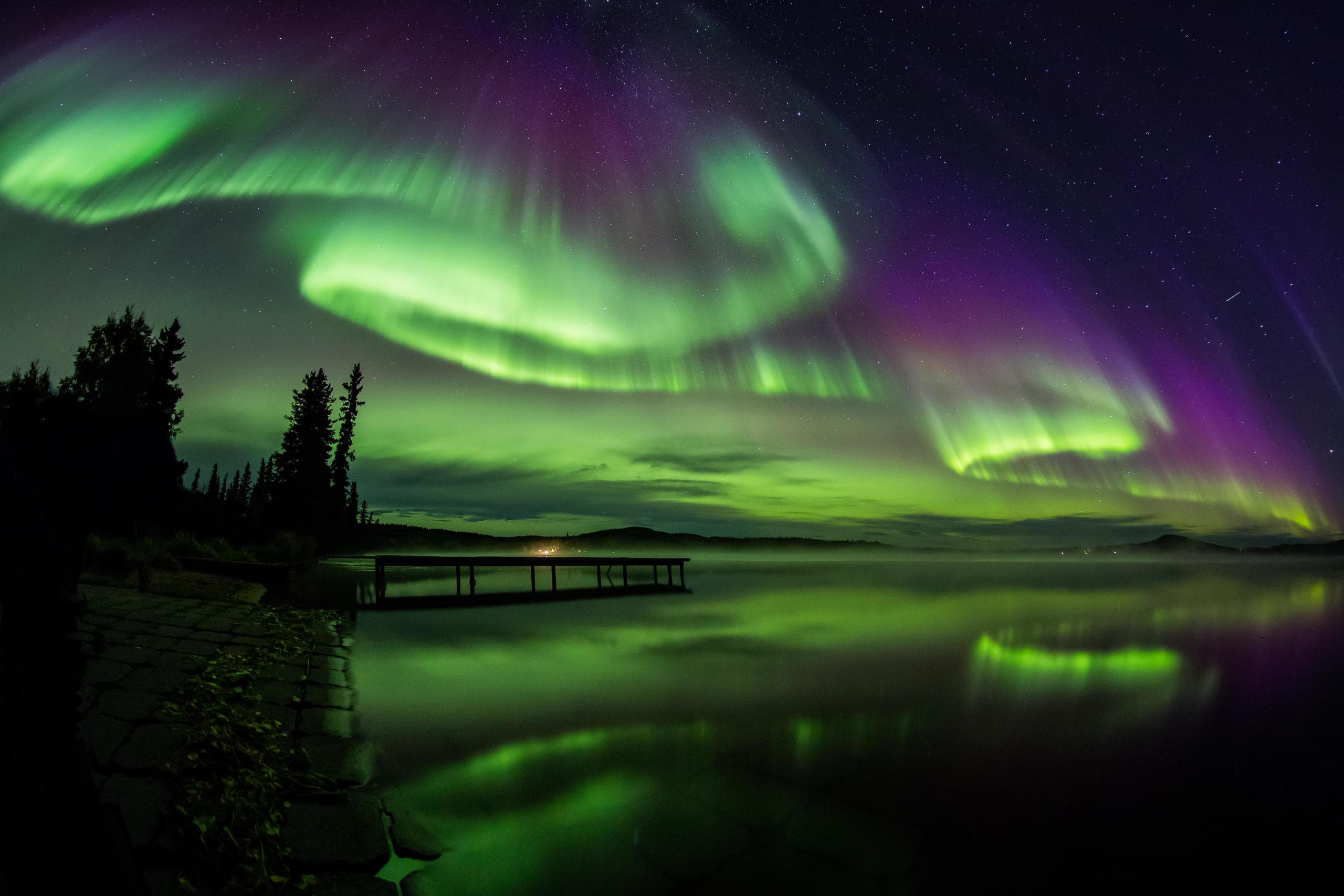 Aurora borealis swirling over frozen lake and dock, nighttime