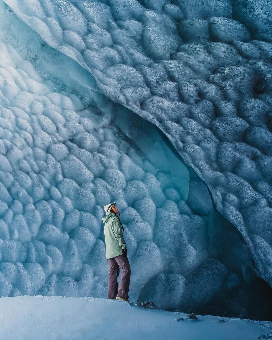 Explorer standing inside blue glacier ice cave admiring formations