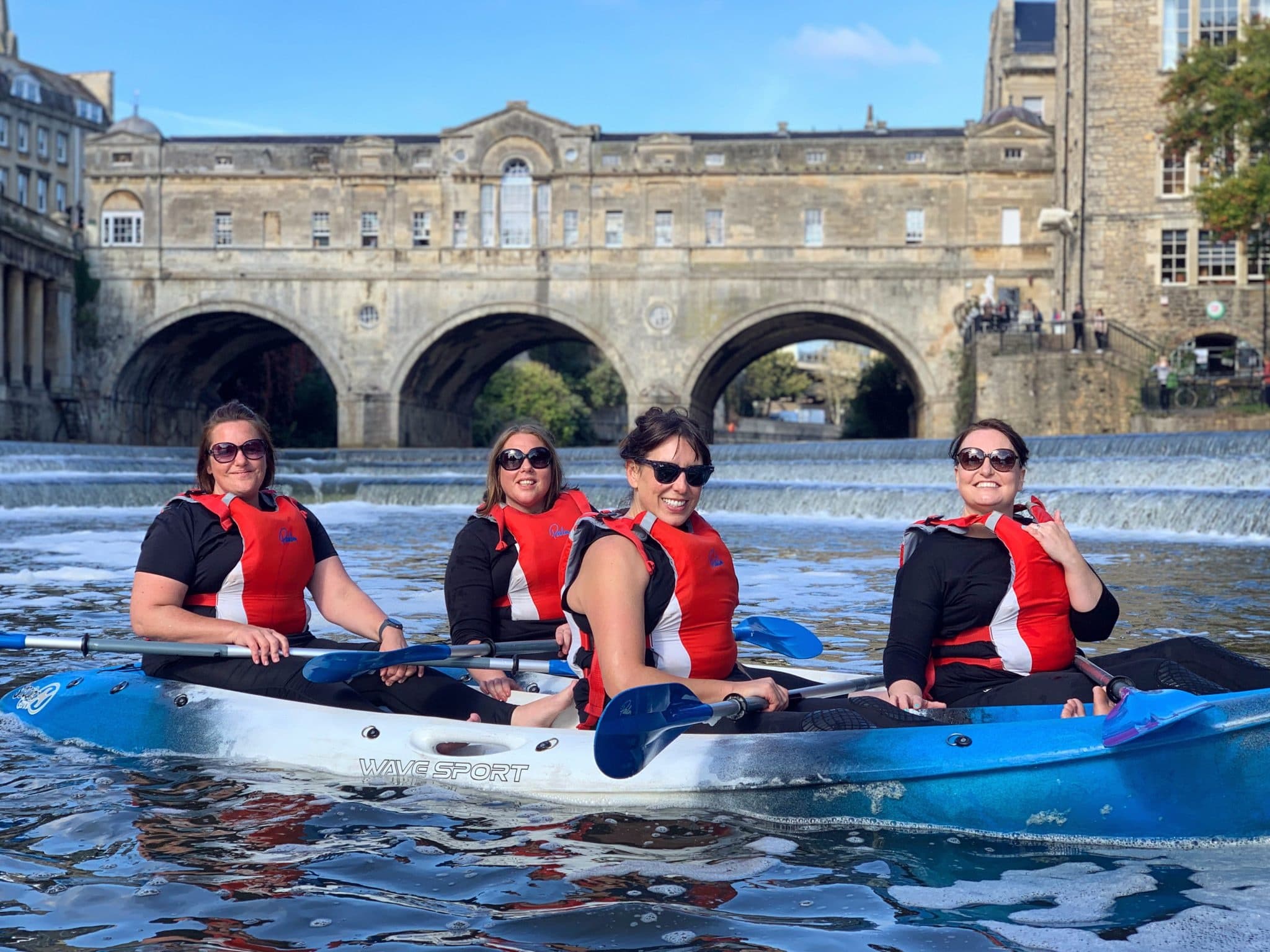 Four kayakers paddling on river by historic arched bridge