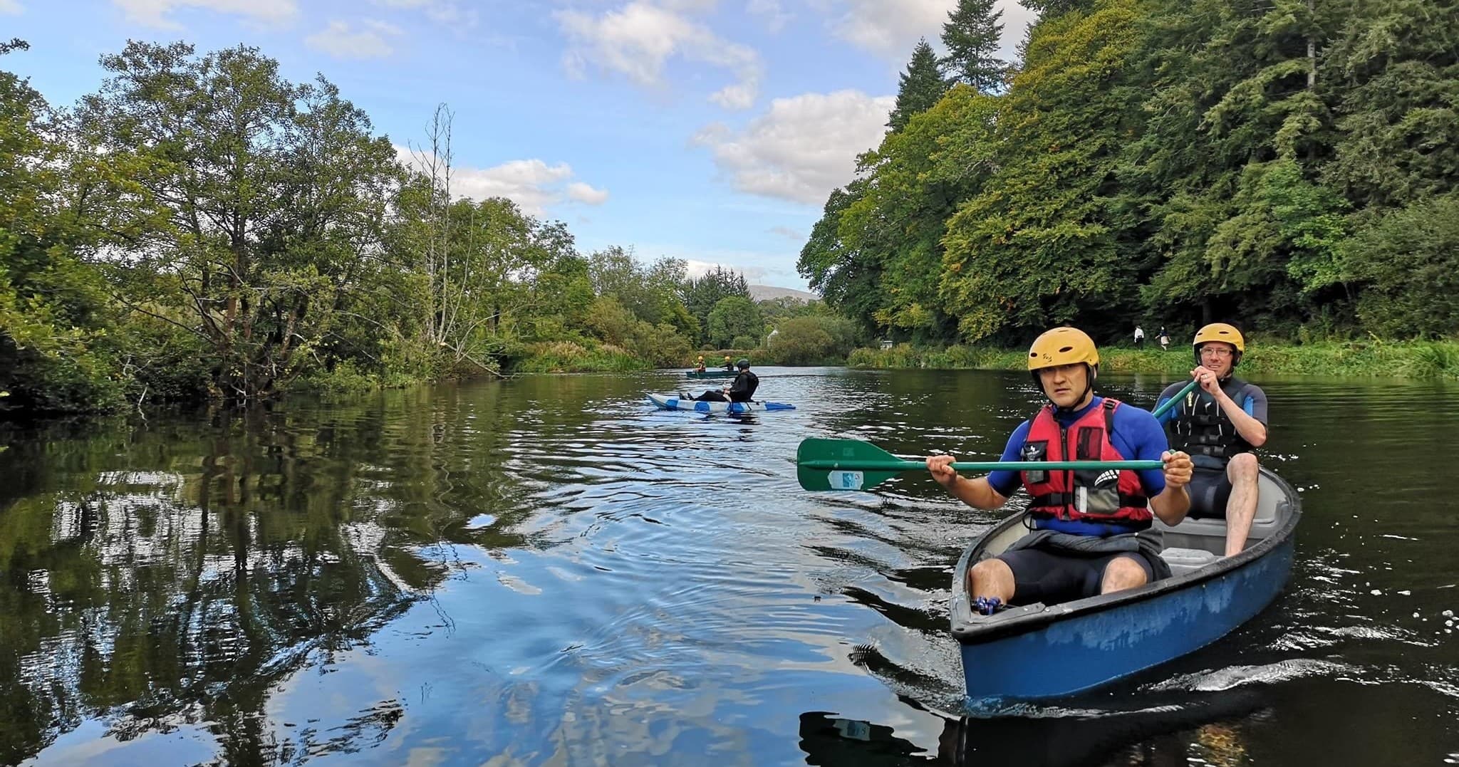 Canoeists paddling a reflective tree-lined river, scenic wilderness