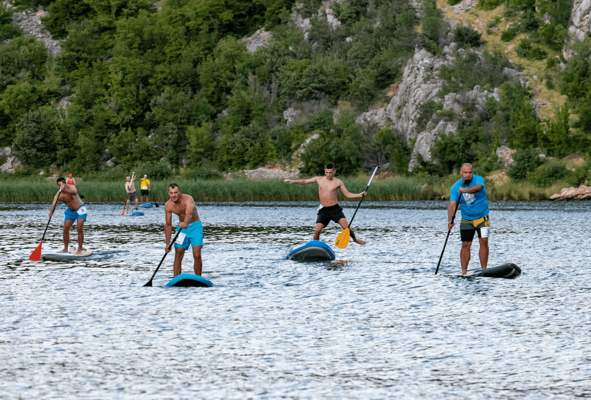 Stand-up paddleboarders crossing a scenic lake with forested shore