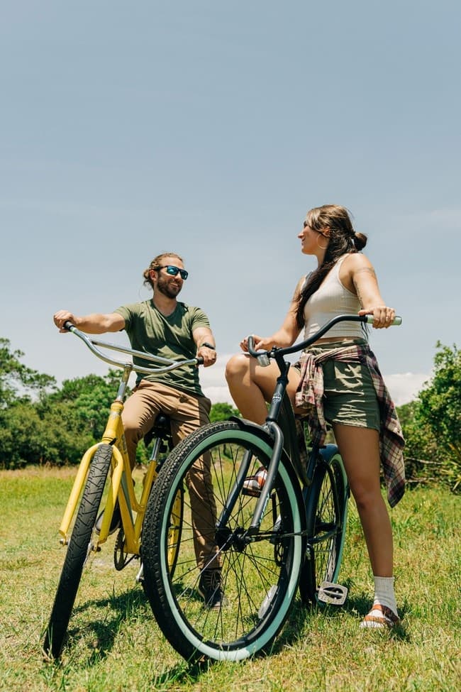 Couple on cruiser bikes in sunny grassy field enjoying bike tour
