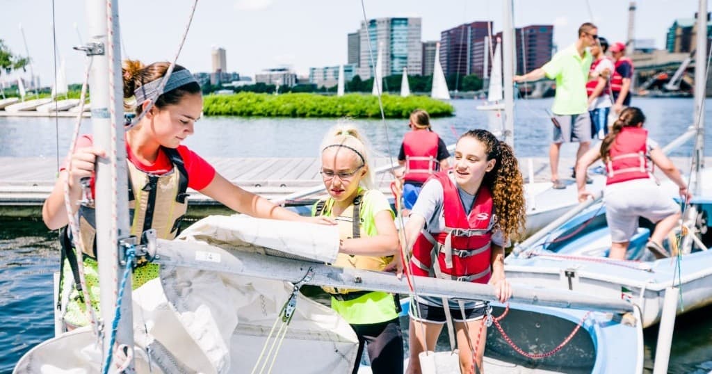 Youth crew prepping sailboats at marina dock, waterfront sailing program
