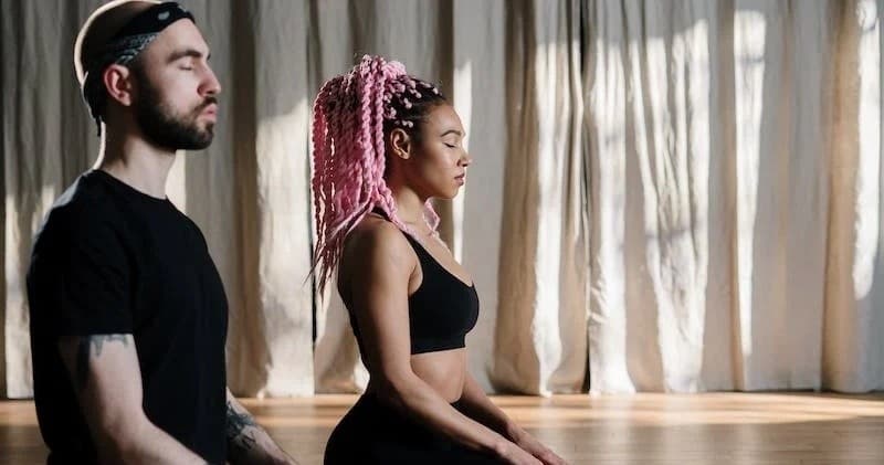 Two people practicing indoor yoga in a studio, seated meditation