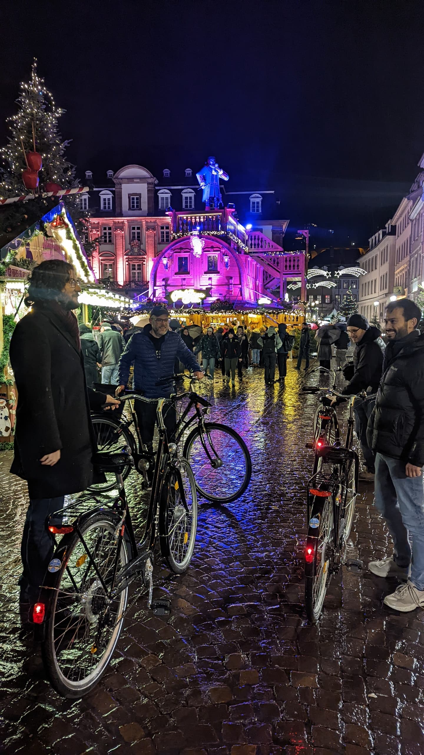 Cyclists walking bikes through crowded illuminated market street at night