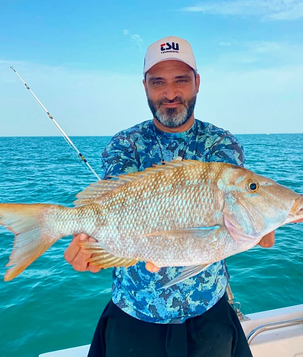 Angler holding large reef fish on turquoise ocean during deep-sea fishing