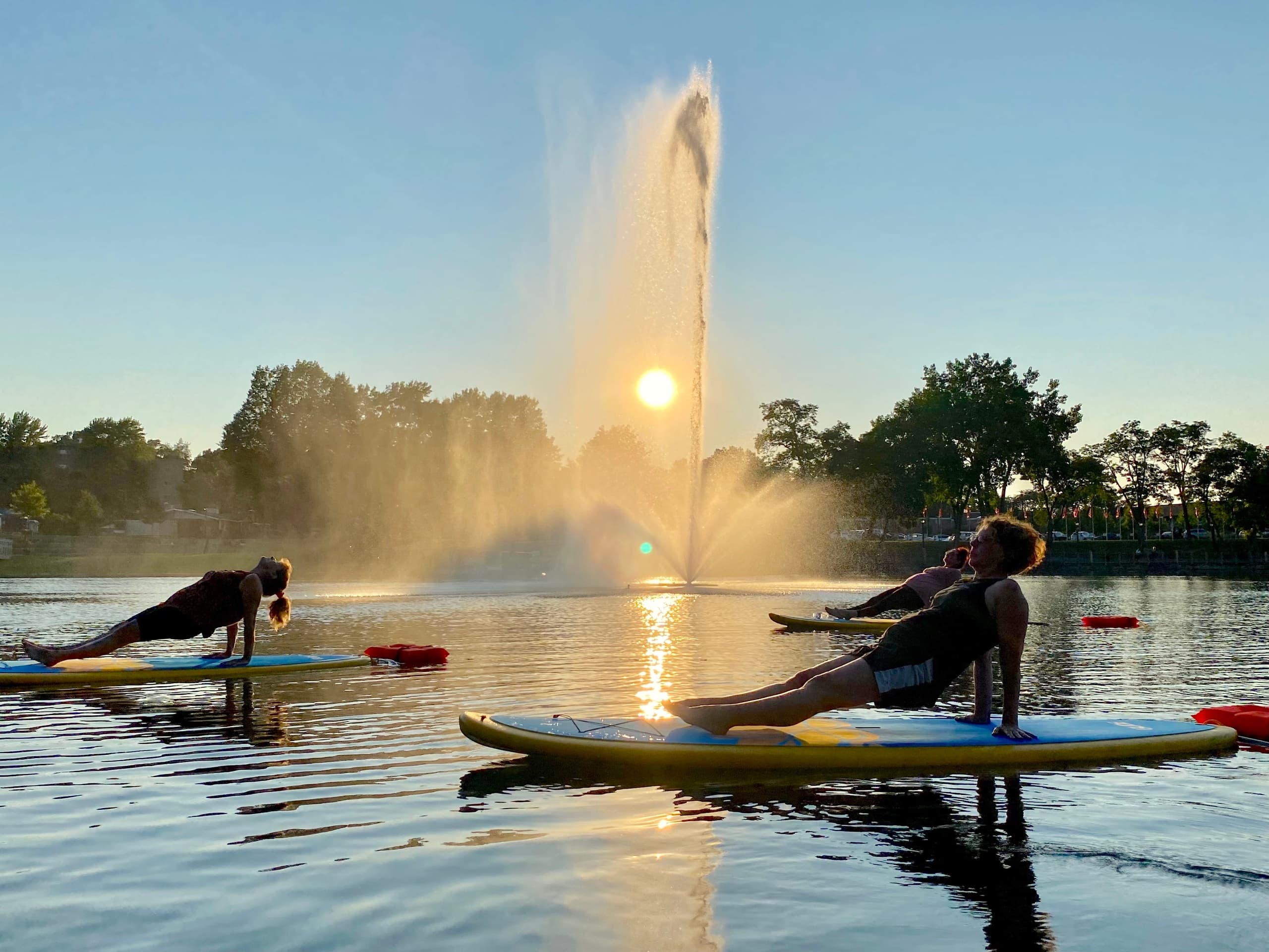 Paddleboard yoga by lake fountain at golden hour with sun flare