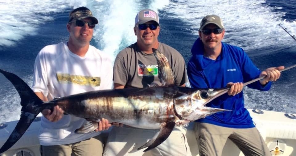 Three anglers posing with marlin on bluewater sportfishing boat