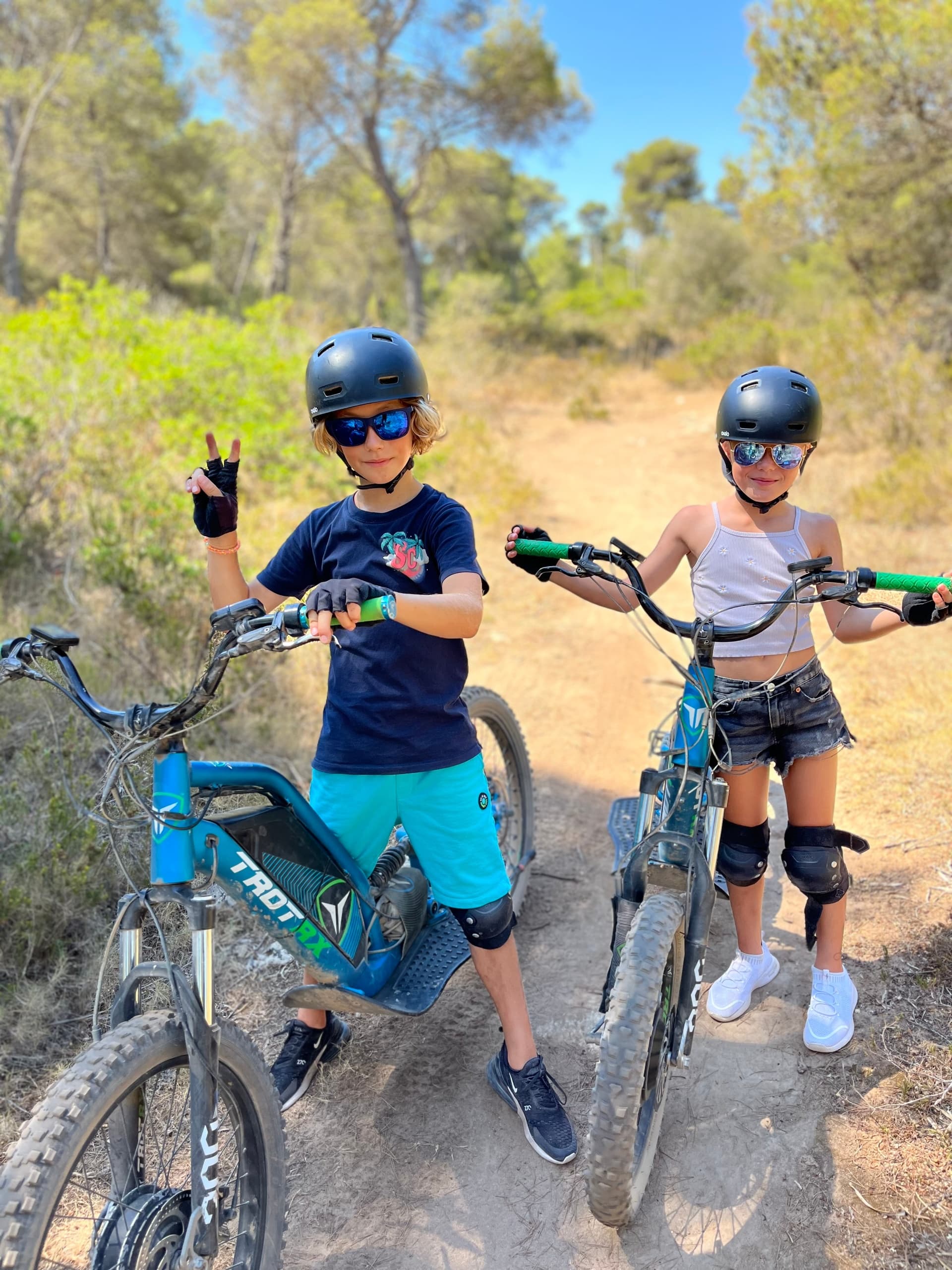 Kids riding electric mountain bikes on dusty forest trail, posing