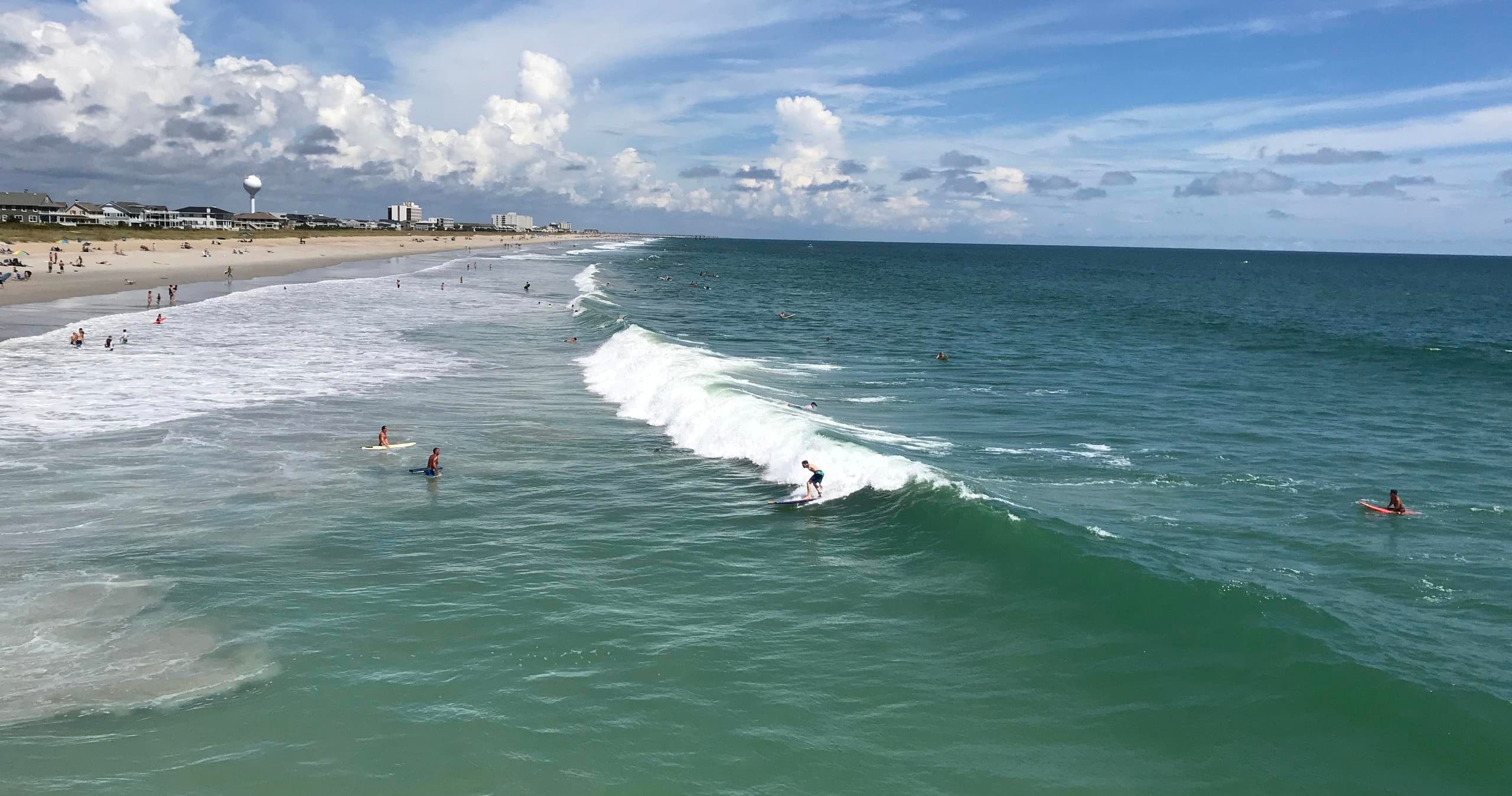 Surfers catching waves near shoreline at sunny coastal beach