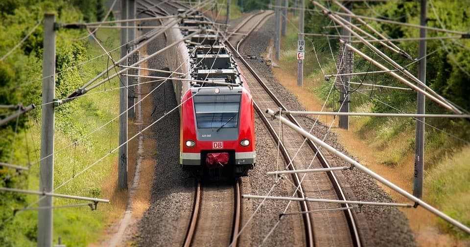 Red passenger train traveling through green countryside tracks