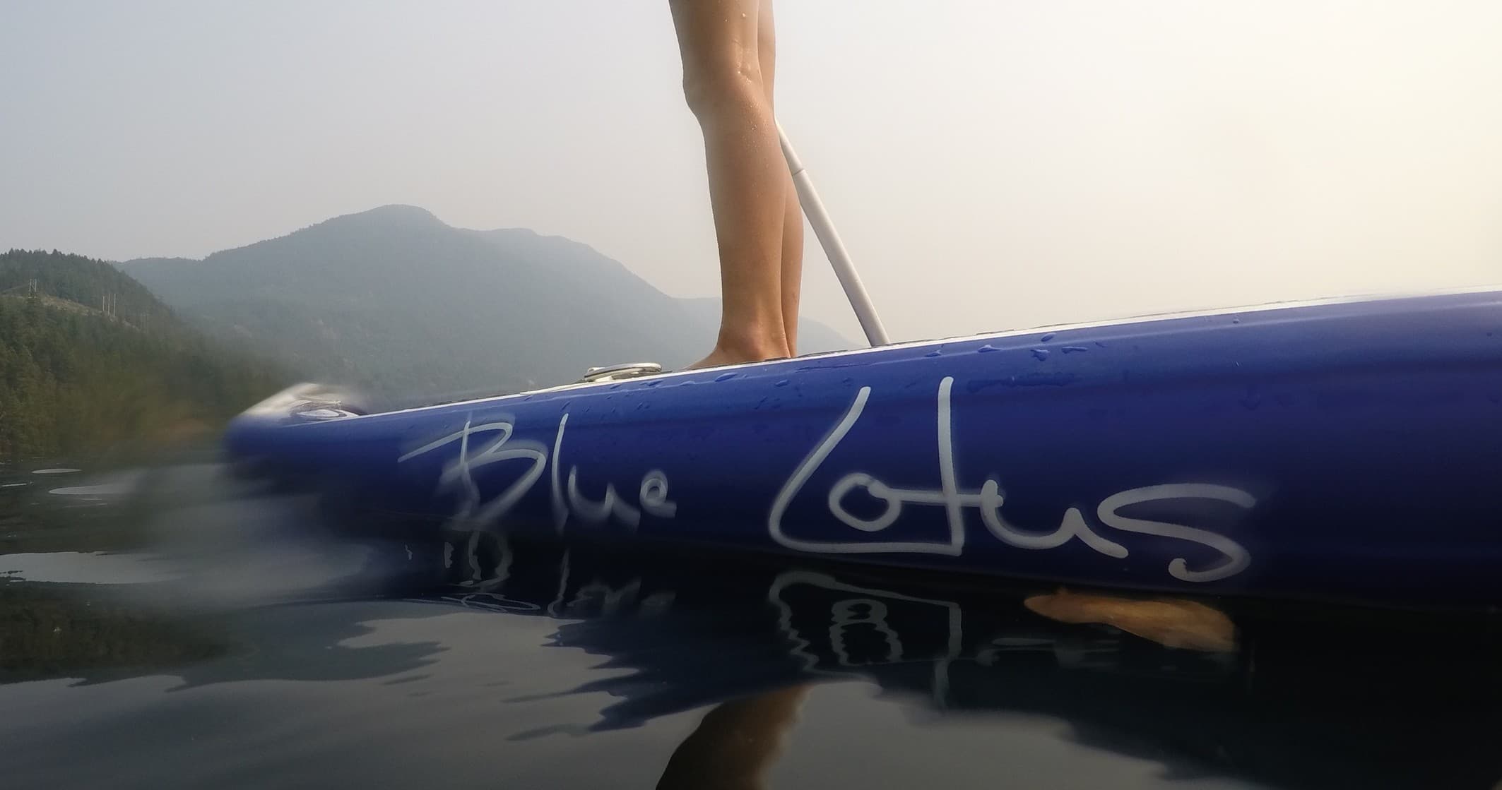 Close-up of paddleboard edge with paddler on calm misty lake