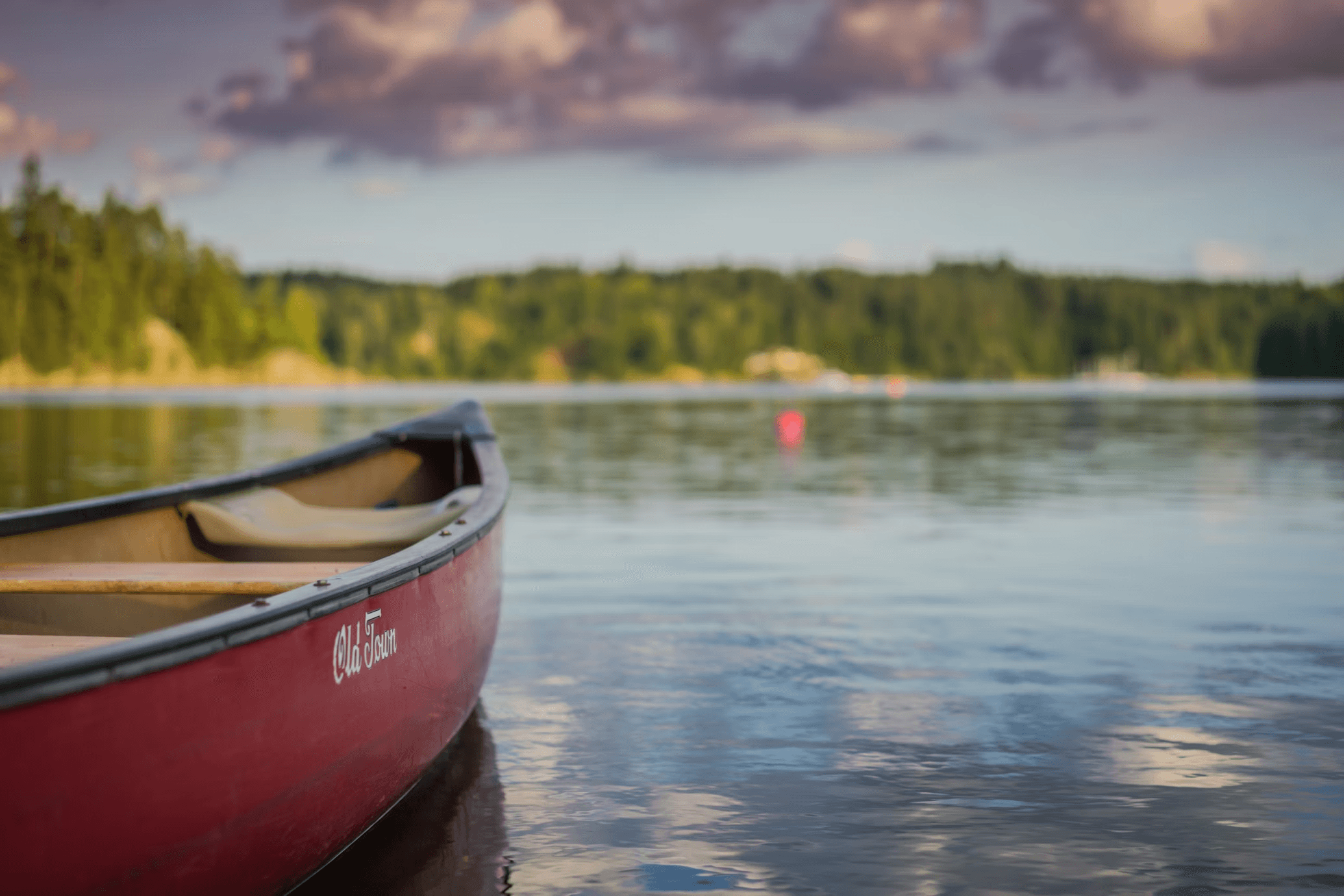 Red canoe moored on calm lake with forested shoreline