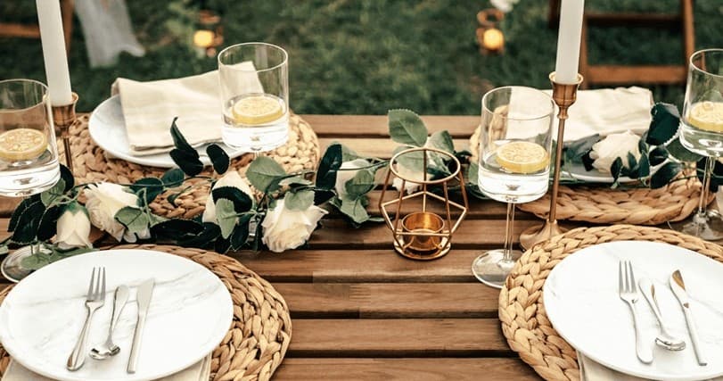 Outdoor wooden dining table with woven placemats on lawn