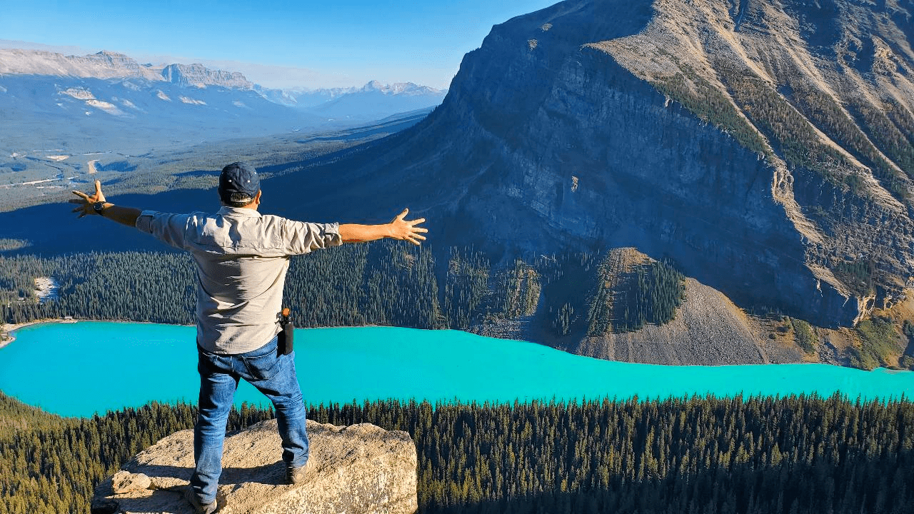 Hiker with arms out overlooking turquoise valley near lake