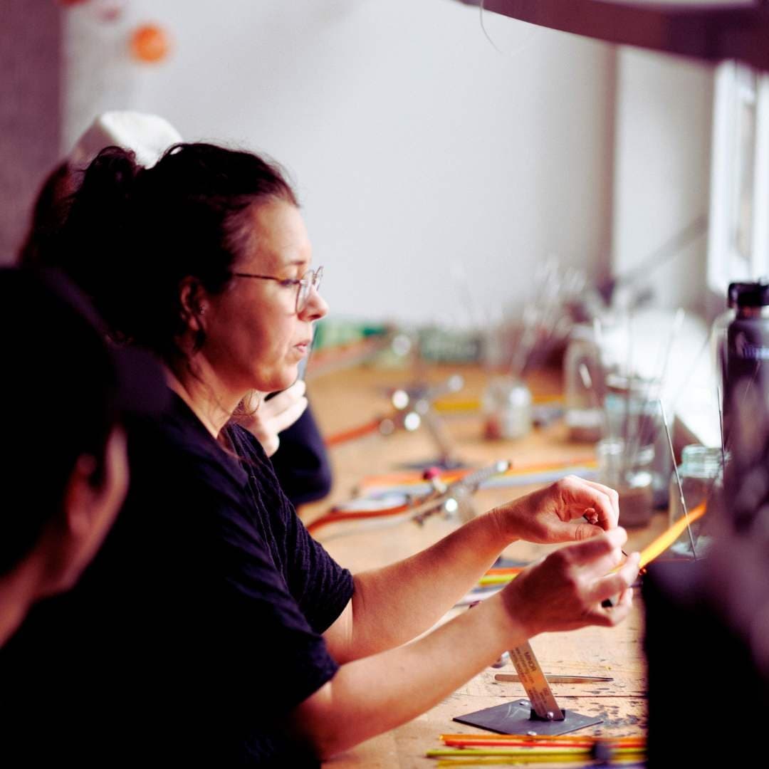 Glass artist at bench crafting pieces in indoor studio workshop