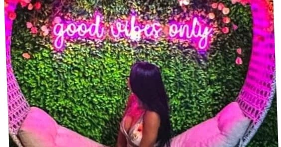 Woman posing on pink swing under neon good vibes sign in studio