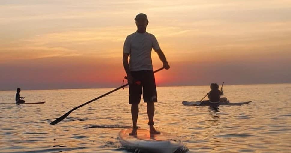 Solo stand-up paddleboarder at sunset on calm Italian sea