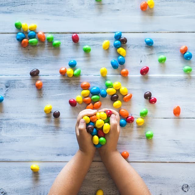 Child hands grabbing colorful candy spread on light wooden table
