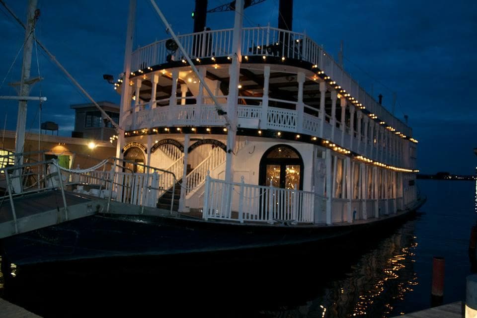 Historic paddlewheel riverboat lit at night docked on riverfront