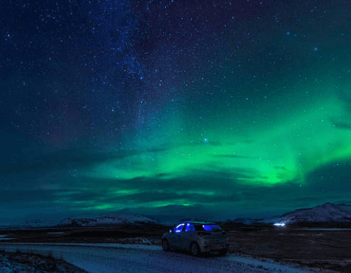 Car parked beneath green northern lights on remote tundra road