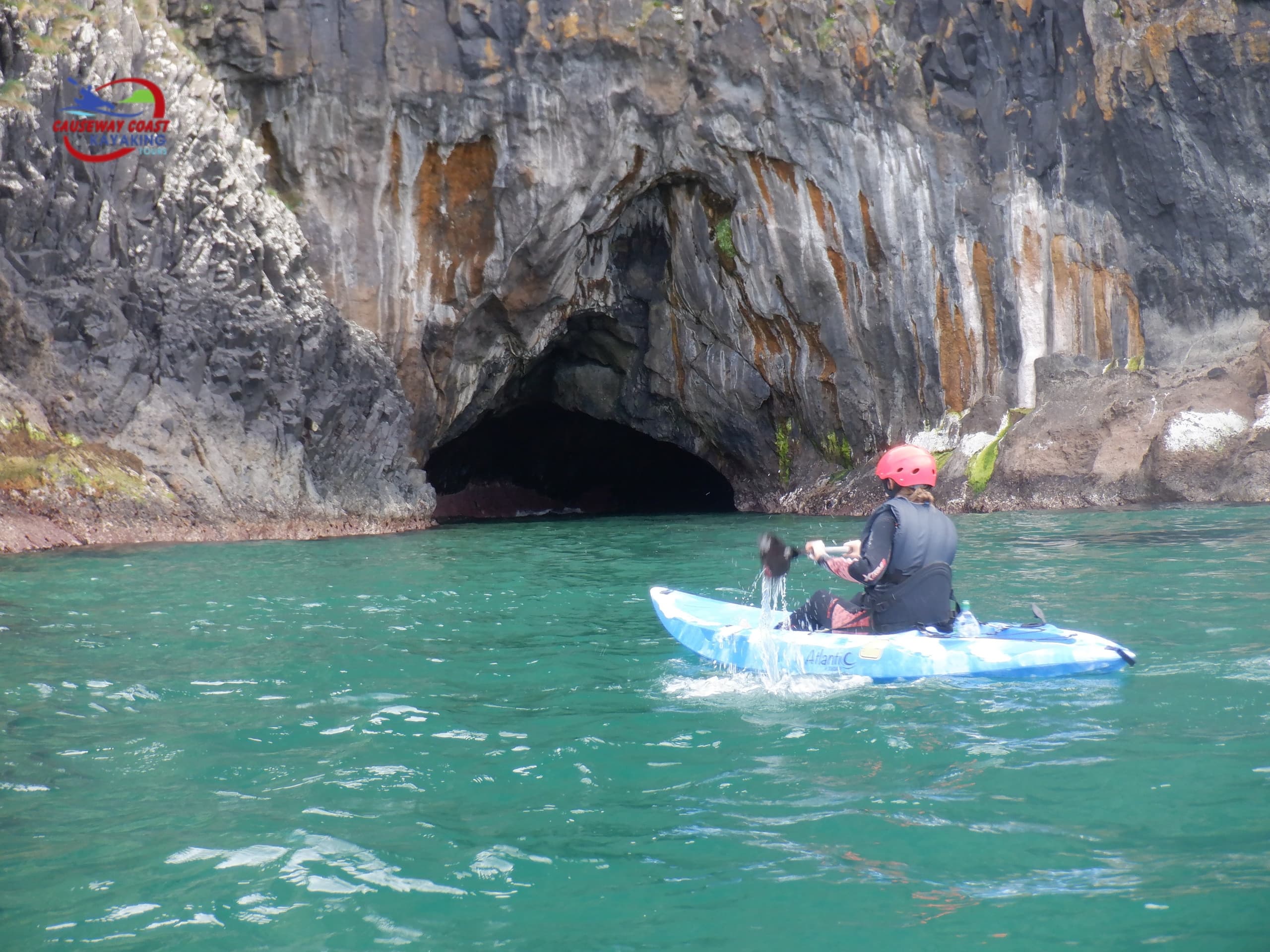 Solo kayaker paddling toward sea cave along rocky Causeway Coast