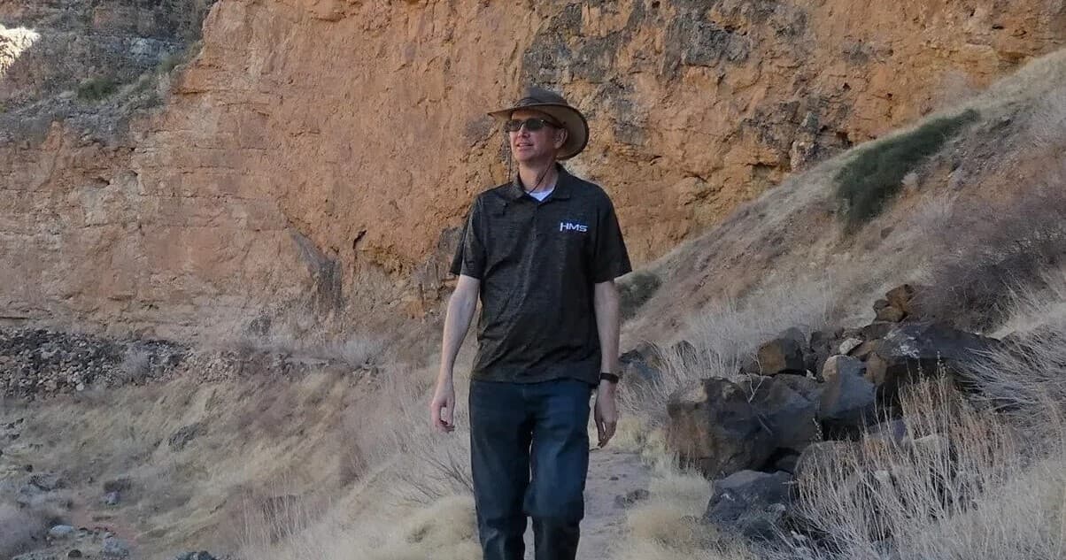 Solo hiker walking along arid canyon trail under sunhat