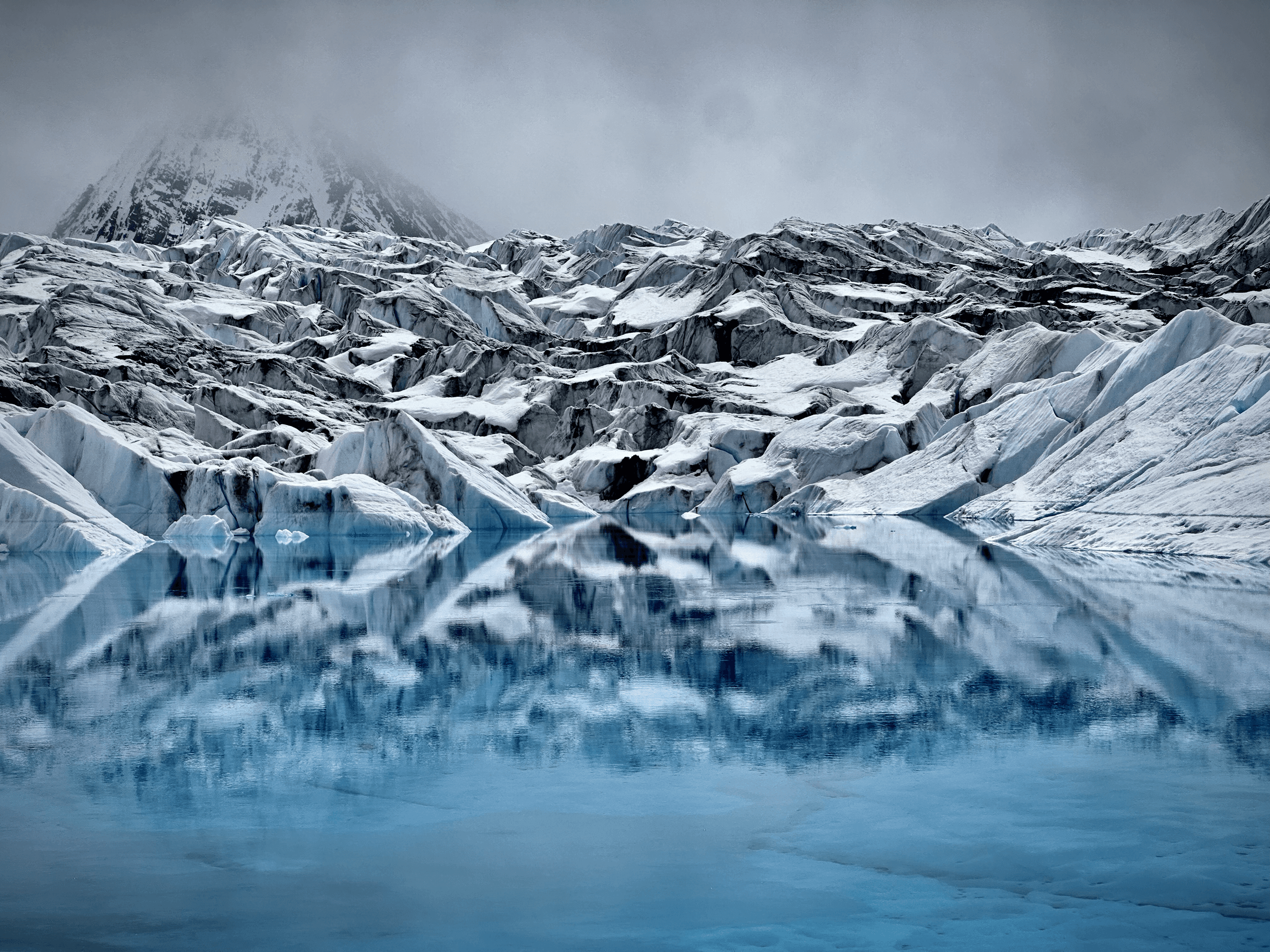 Moody crevassed glacier reflected in icy meltwater, alpine setting