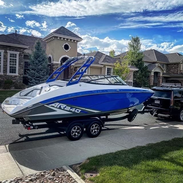 Black wake boat on trailer with blue sky and neighborhood backdrop
