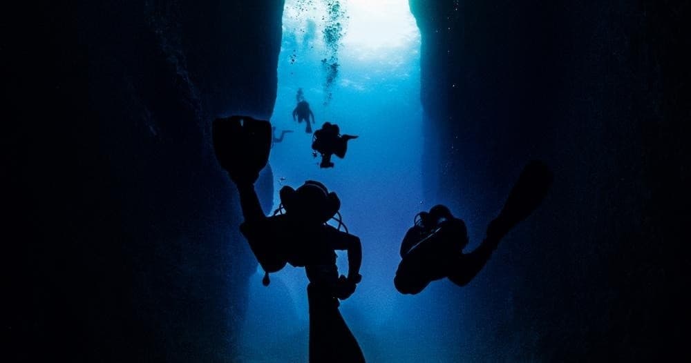 Scuba divers silhouetted exploring dramatic underwater cave passage