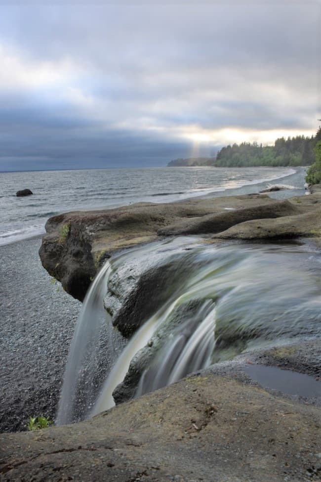 Seaside waterfall pouring over sandstone ledge onto pebble beach